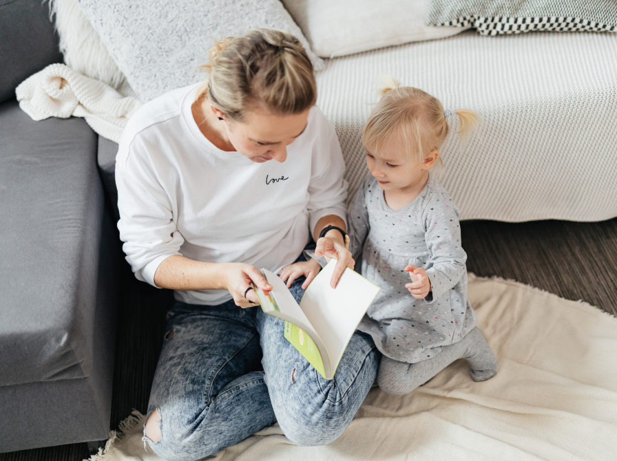 Kvinde læser højt for pige på tæppe